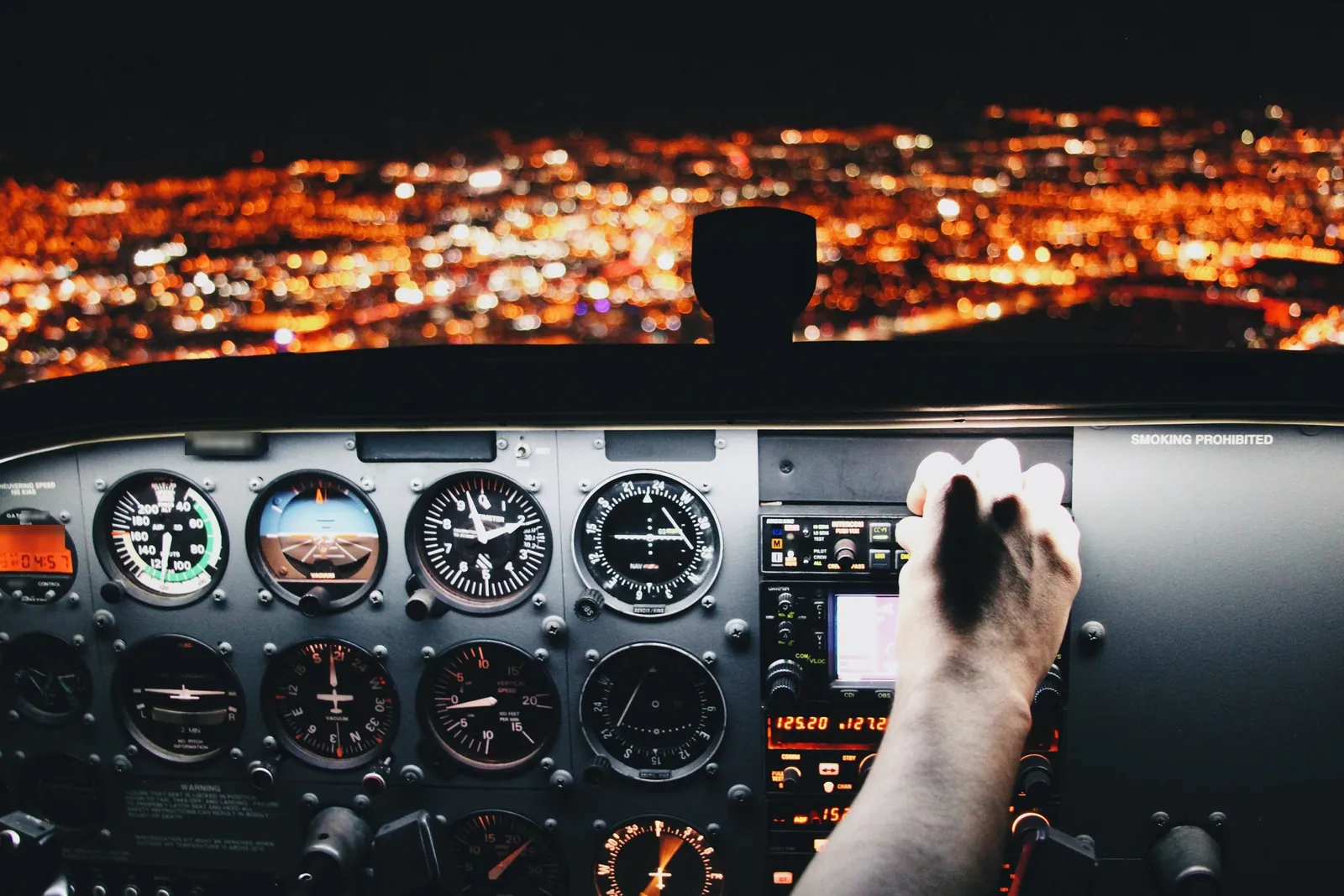 A pilot's hand on the controls of a small aircraft above city lights at night