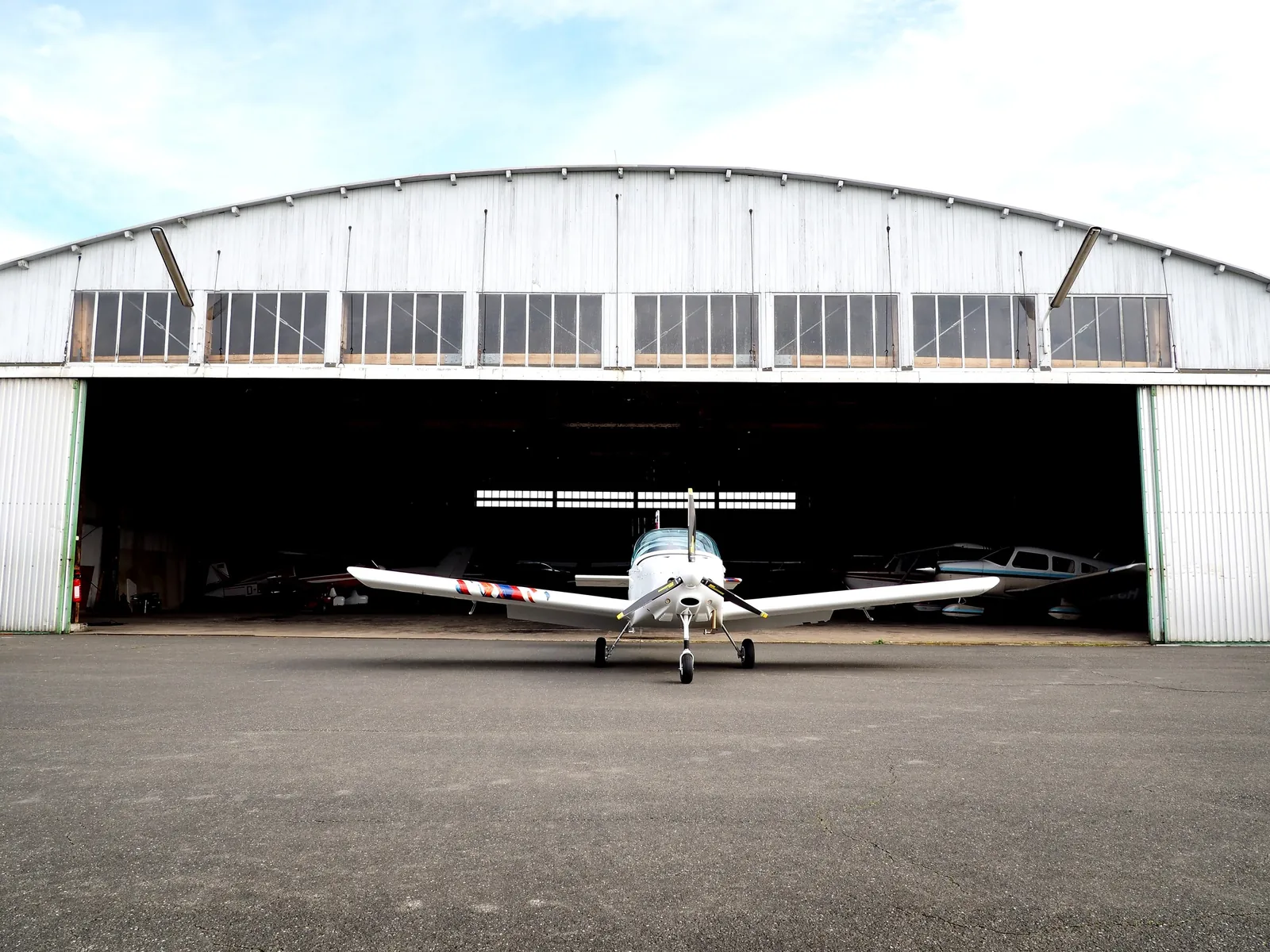 A light aircraft parked in front of an open hangar
