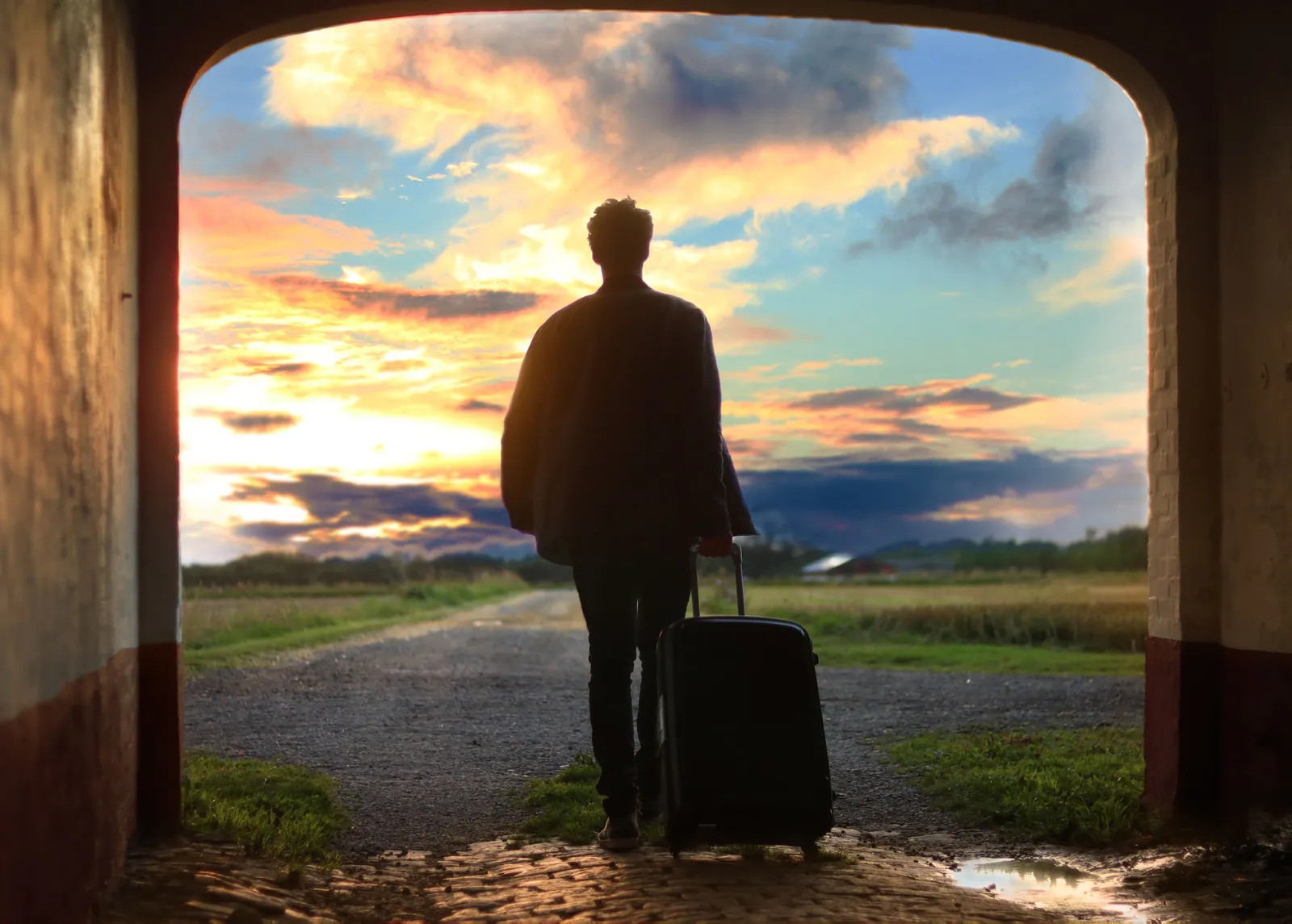 A traveller with a suitcase walking out into a sunset landscape