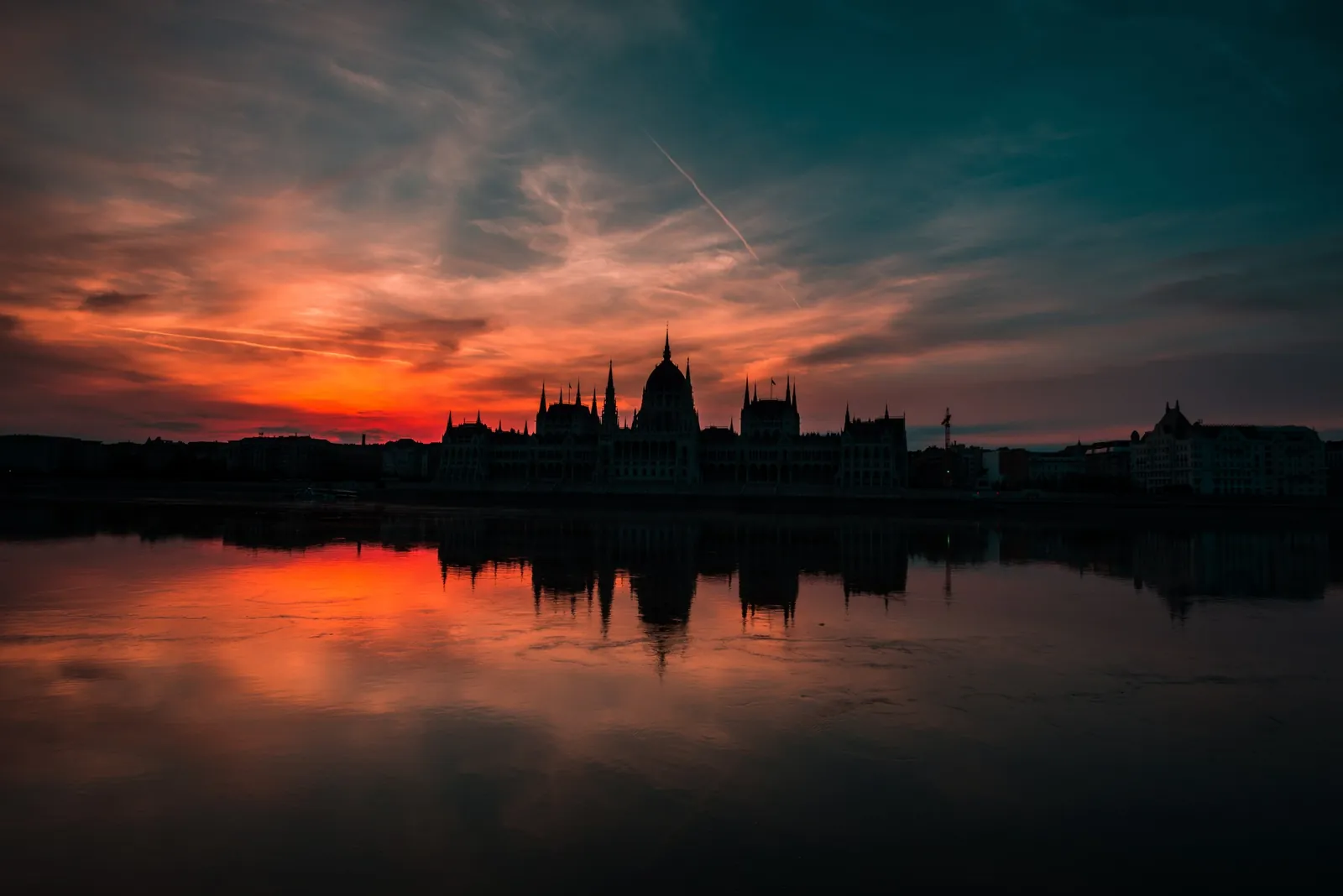 A parliament building in silhouette against a red sunset, with its reflection in water