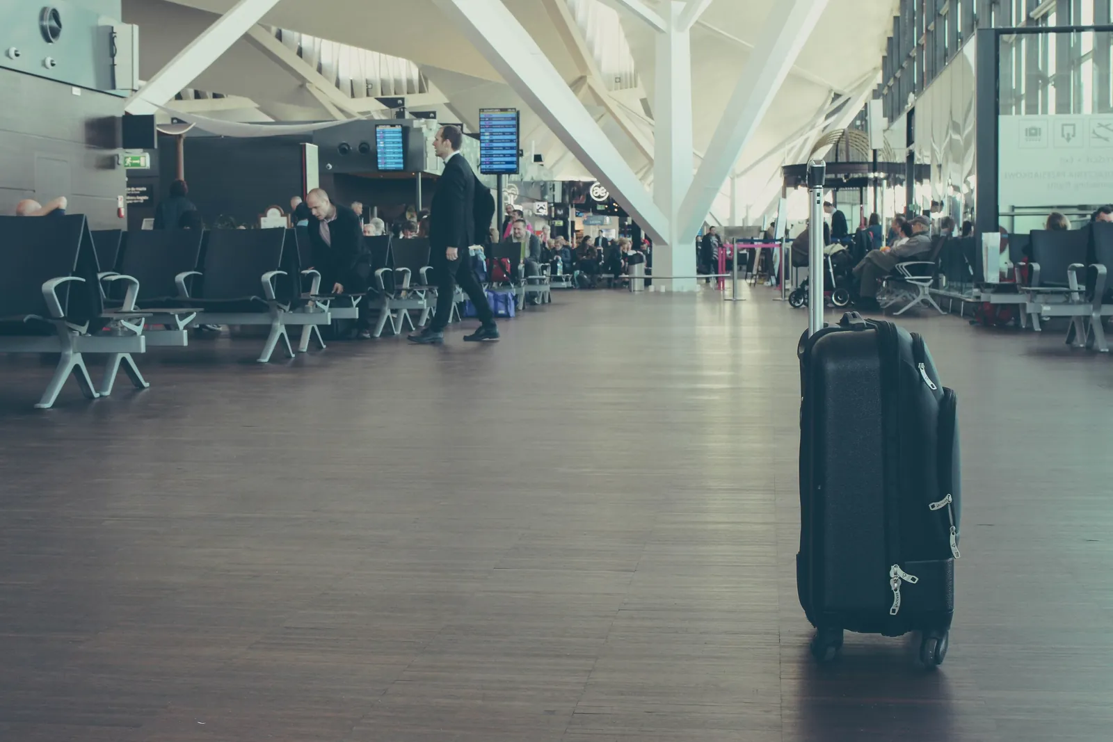 A busy airport departure hall with a suitcase in the foreground