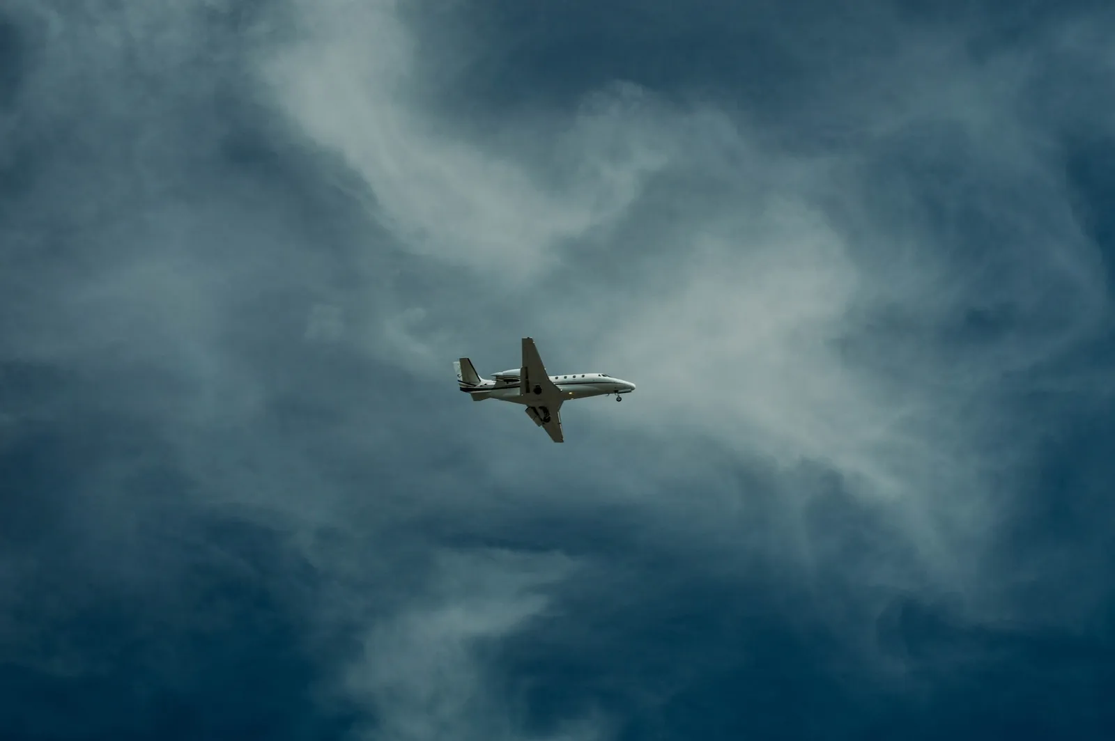 A small business jet flying through a dark, cloudy sky