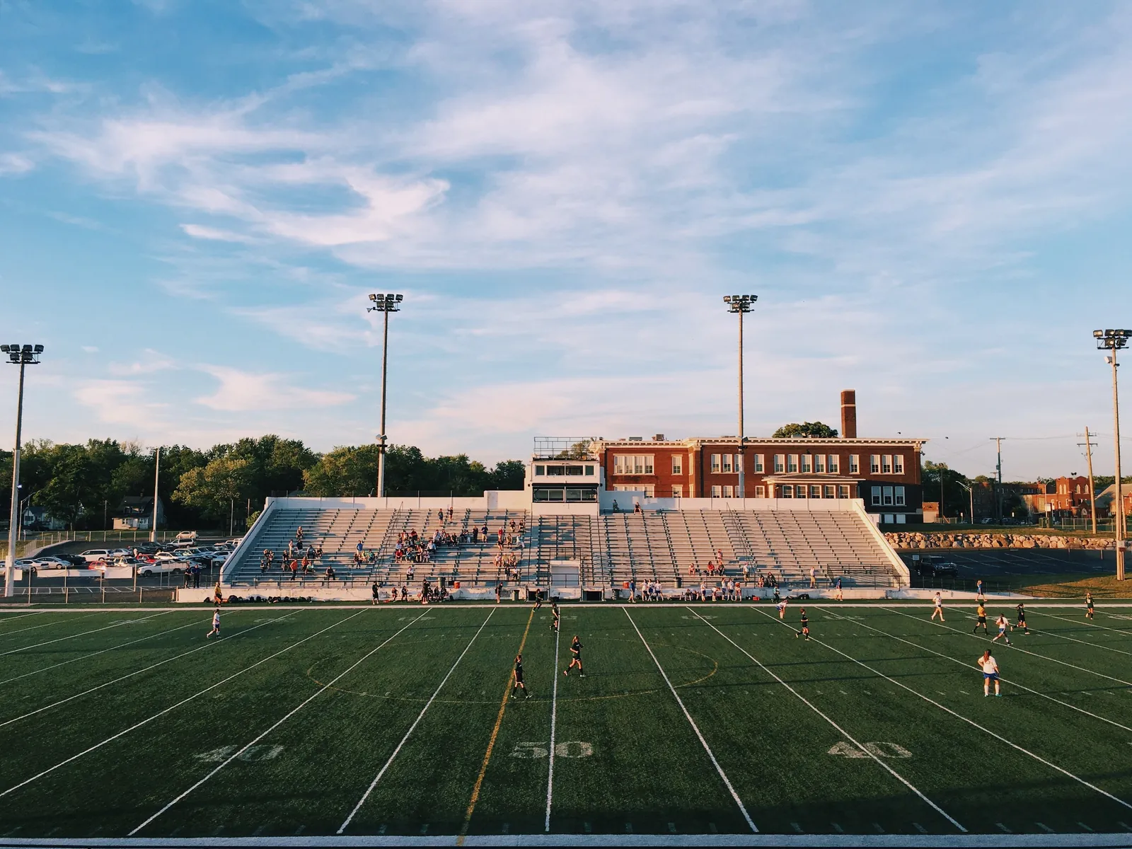 A floodlit football pitch with players and a stand beyond