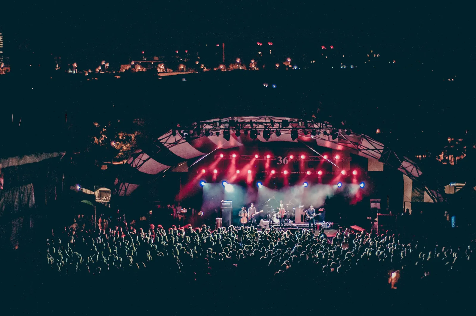 A crowd watching a lit stage at an outdoor evening concert